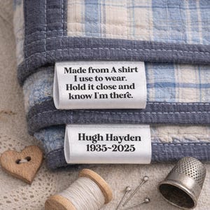 May include: A blue and white plaid fabric with a dark blue border, featuring two white labels. The top label reads, "Made from A shirt I use to wear. Hold it close and know I'm there." The bottom label says "Hugh Hayden 1935-2025."