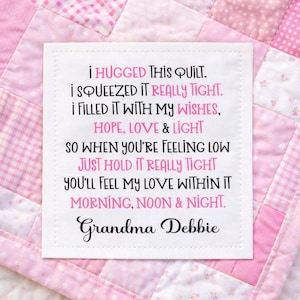 May include: A pink and white patchwork quilt with a white square label. The label features a poem in black and pink text, signed "Grandma Debbie."