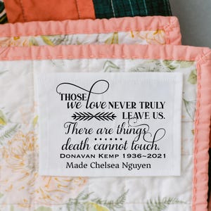 May include: A white fabric label with black text is sewn onto a floral quilt. The label reads "Those we love never truly leave us. There are things death cannot touch." It includes a name and dates.
