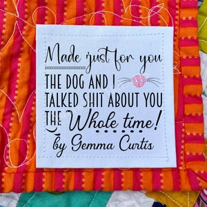 May include: A white fabric label with black text that reads "Made just for you THE DOG AND I TALKED SHIT ABOUT YOU THE Whole time! by Gemma Curtis." The label is on a colorful quilt with orange, pink, and green patterns.
