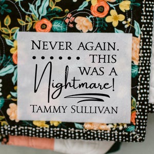 May include: A handmade quilt with a floral pattern in orange, yellow, and green on a black background. The quilt features the text "NEVER AGAIN. THIS WAS A Nightmare!" and the name "TAMMY SULLIVAN".