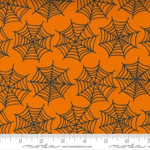 May include: Orange fabric with a black spiderweb pattern. The fabric is measured with a ruler in inches.