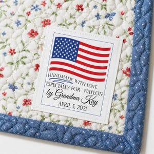May include: A quilted textile with a floral pattern in red and blue on a white background. A label with the American flag and text that reads "Handmade with Love especially for Waylon by Grandma Kay April 5, 2021" is sewn on the quilt.