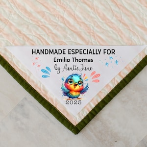 May include: A handmade quilt with a label that reads "HANDMADE ESPECIALLY FOR Emilio Thomas by Auntie June". The label features a colorful cartoon bird and the year 2025. The quilt has a pink and white striped pattern.