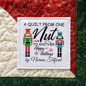May include: A square quilt label with the text "A Quilt From One Nut To Another Happy Holidays by Norma Tilford". The label features illustrations of two toy soldiers and holiday-themed graphics.