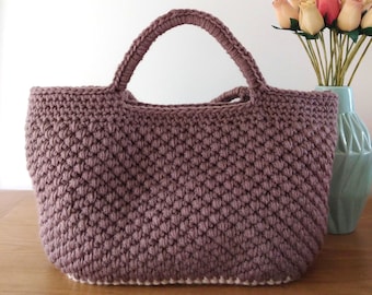 May include: A crocheted tote bag with a brown color and a white trim. The bag has a wide, rounded bottom and two handles.
