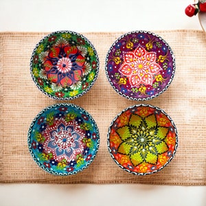 Op de afbeelding: Vier kleurrijke keramische kommen met ingewikkelde bloemmotieven. De kommen zijn in een vierkant patroon op een bruine jute ondergrond gerangschikt.