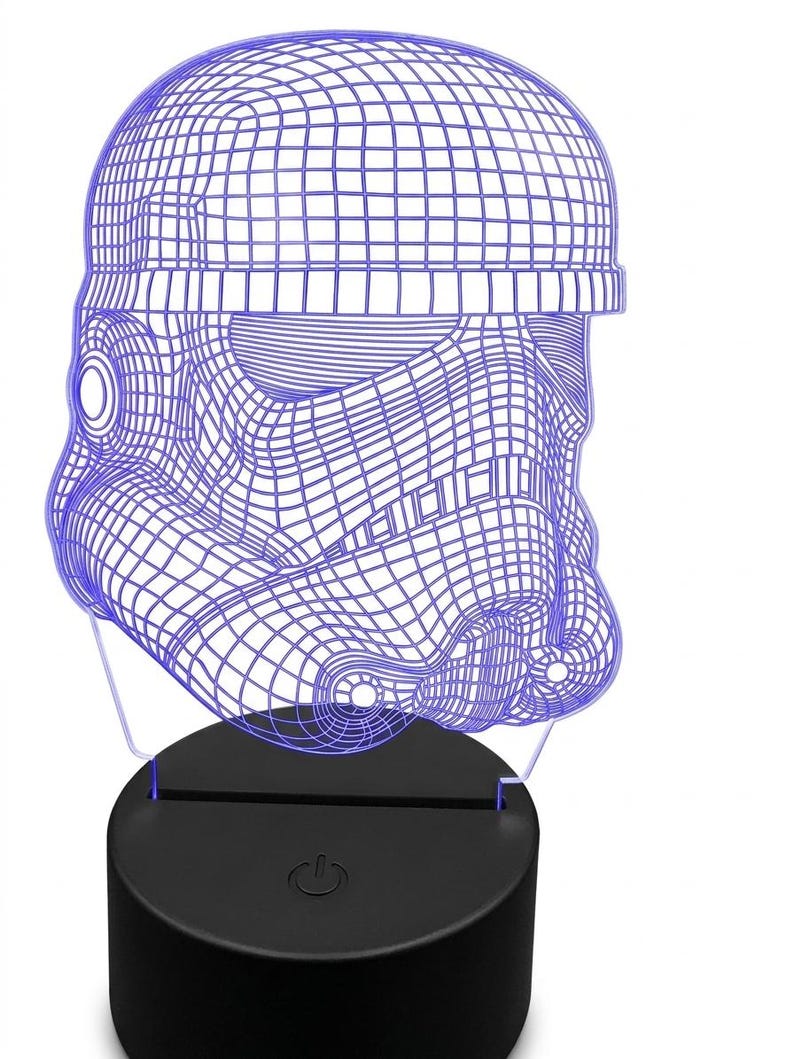May include: A blue wireframe Stormtrooper helmet night light. The helmet is illuminated with a blue glow and sits atop a black base with a power button. The design is a 3D illusion, creating a unique decorative piece.