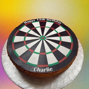May include: A round cake decorated with a black and white dartboard design. The cake is inscribed with the text "Happy 15th Birthday Charlie".