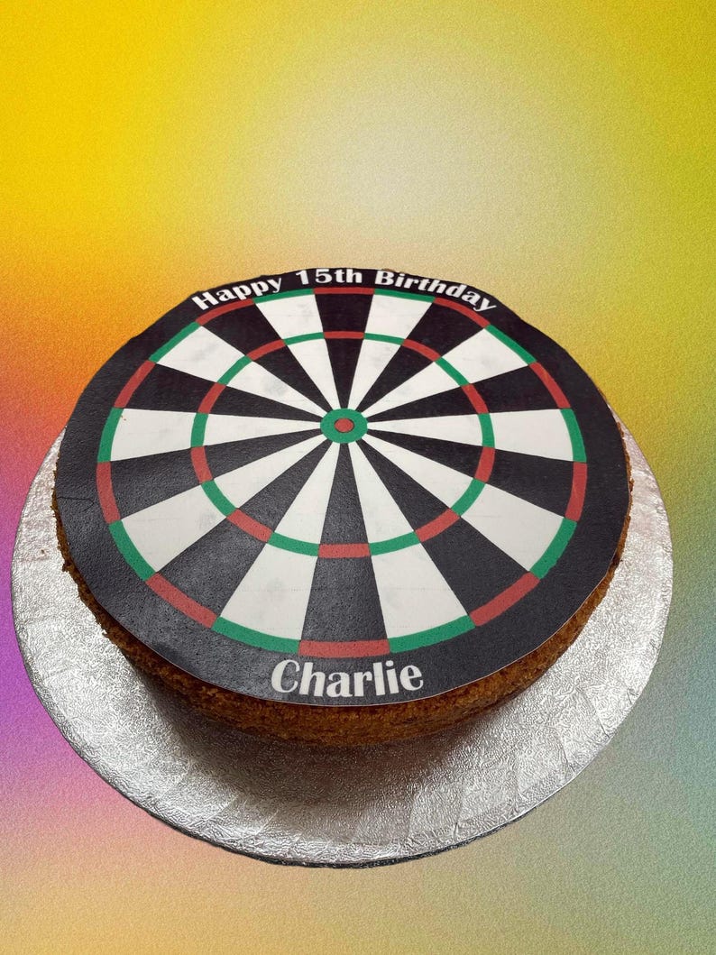 May include: A round cake decorated with a black and white dartboard design. The cake is inscribed with the text "Happy 15th Birthday Charlie".