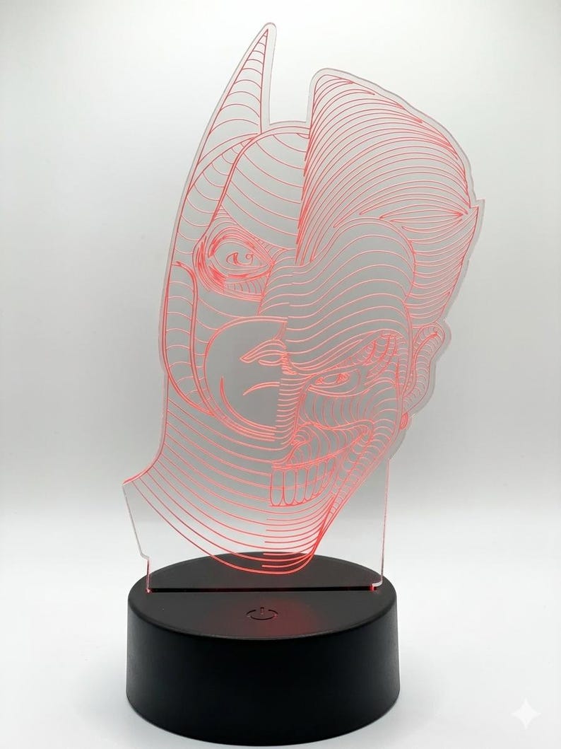 May include: A red-lined Batman head design is illuminated by a black base. The acrylic art piece features a detailed outline of the superhero's mask and cowl. The base has a power button and a small light.