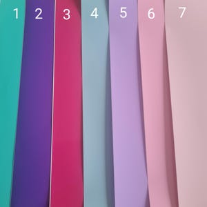 May include: A close-up shot of seven vertical strips of colored paper. The colors include teal, purple, magenta, light blue, lavender, pink, and light pink. The strips are arranged side by side, creating a vibrant and colorful display.