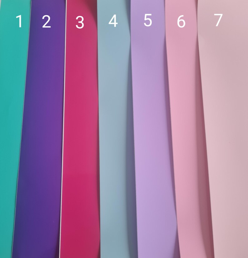 May include: A close-up shot of seven vertical strips of colored paper. The colors include teal, purple, magenta, light blue, lavender, pink, and light pink. The strips are arranged side by side, creating a vibrant and colorful display.