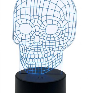 May include: A blue wireframe skull-shaped LED lamp. The skull design is a grid of blue lines, with eye and nose openings. The lamp sits on a black, cylindrical base that emits a soft blue glow.