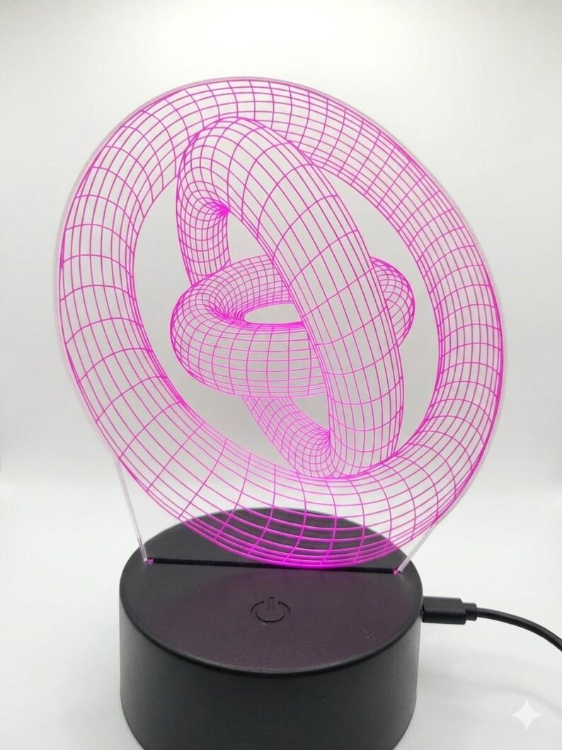 May include: A pink 3D-printed geometric sculpture illuminated by an LED light. The sculpture features a complex, interwoven design, mounted on a black base with a power button. A USB cable extends from the base.