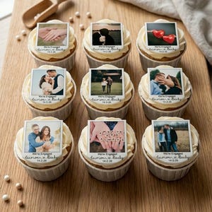 May include: Nine cupcakes with white frosting, each topped with a small photo. The photos depict engagement-themed images. Text on the photos reads "We're Engaged" and a date. The cupcakes sit on a wooden board with a wooden scoop.