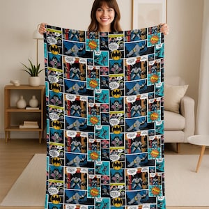 May include: A rectangular Batman comic book-themed blanket. The blanket features a black background with comic book panels in shades of blue, yellow, and purple. The panels depict Batman in action, with speech bubbles and the word "POW".