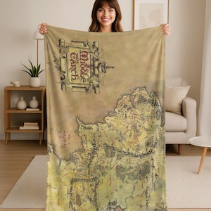 May include: A beige blanket featuring a detailed map of Middle Earth, with the words "Middle Earth" in a decorative banner. The map includes geographical features and text, with a vintage aesthetic.