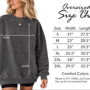 May include: A woman wearing a dark gray oversized sweatshirt. The image includes a size chart with measurements in inches for width, length, and sleeve length. The chart ranges from size S to 3XL.