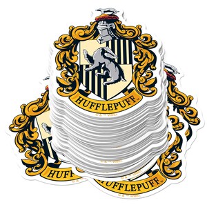 May include: A stack of Hufflepuff crest stickers. The crest features a badger, a shield with black and yellow stripes, and the words "HUFFLEPUFF" in gold lettering. The stickers have a white background and are from the Harry Potter series.