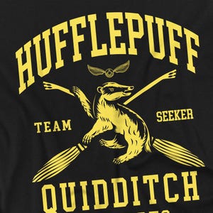May include: Black t-shirt featuring a yellow Hufflepuff Quidditch design. The design includes a badger, crossed brooms, and the words "Hufflepuff", "Team", "Seeker", and "Quidditch". A golden snitch is also present.