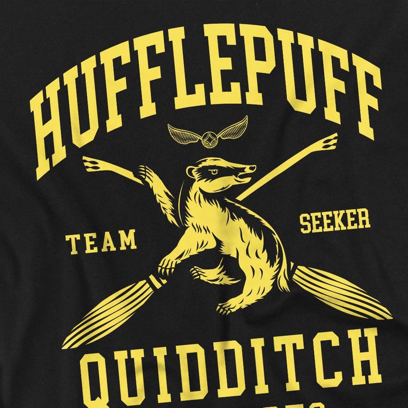 May include: Black t-shirt featuring a yellow Hufflepuff Quidditch design. The design includes a badger, crossed brooms, and the words "Hufflepuff", "Team", "Seeker", and "Quidditch". A golden snitch is also present.