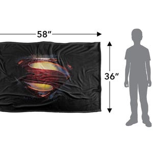 Puede incluir: Manta negra con el logotipo de Superman en rojo, amarillo y azul. La manta mide 147 cm de largo y 91 cm de ancho. Se muestra una silueta de 122 cm para dar una idea de la escala.
