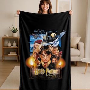 May include: Black fleece blanket featuring the Harry Potter movie poster for "Sorcerer's Stone." The design includes the movie title, characters, and a snowy owl. The words "Let the Magic Begin" are at the top.