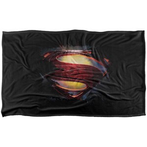 Puede incluir: Manta negra con el logotipo de Superman en rojo, amarillo y azul. El logotipo tiene un aspecto desgastado y usado. La manta es rectangular y est&aacute; hecha de un material suave.