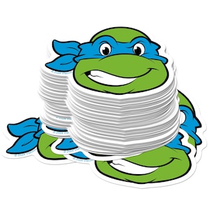 May include: A stack of Leonardo Teenage Mutant Ninja Turtle stickers. The stickers feature a green turtle head with a blue mask and a smiling expression. The stickers are white with a glossy finish and a die-cut shape.