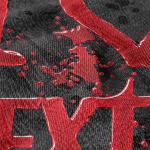 May include: Close-up of a black fabric with red text and splatters. The red text appears to be part of a larger word, with a glossy, dripping effect. The fabric has a textured appearance.