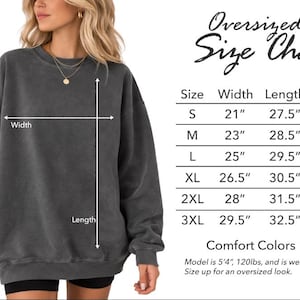 May include: A woman wearing a dark gray oversized sweatshirt. The image includes a size chart with measurements in inches for width, length, and sleeve length. The sweatshirt is Comfort Colors 1566.