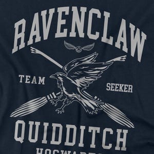 May include: Navy blue t-shirt featuring a Ravenclaw Quidditch design. The design includes the text "RAVENCLAW", "TEAM", "SEEKER", and "QUIDDITCH" in white, along with a raven, a snitch, and crossed brooms. The shirt is a fan item.