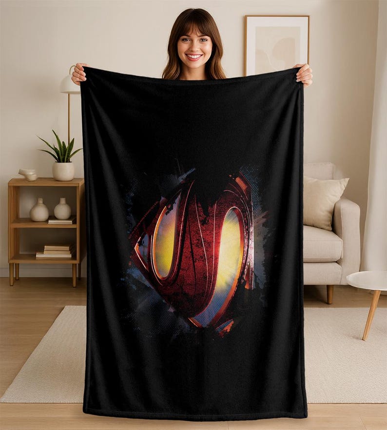 Puede incluir: Manta de forro polar negra con el logotipo de Superman desgastado en rojo, amarillo y azul. La manta est&aacute; sostenida por una persona, mostrando su tama&ntilde;o y dise&ntilde;o. Un art&iacute;culo de decoraci&oacute;n del hogar acogedor.