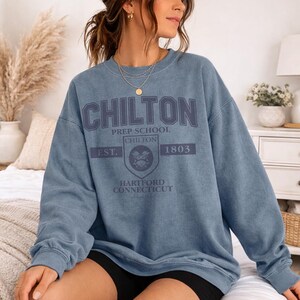 May include: A blue crewneck sweatshirt with the text "CHILTON PREP SCHOOL" in a dark blue font. The sweatshirt also features a crest with the text "CHILTON EST. 1803 HARTFORD CONNECTICUT". The sweatshirt is a solid blue color.