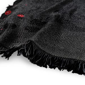 May include: A close-up of a black round beach towel with a fringed edge. The towel has a textured appearance and several red droplets are visible on the surface. The towel is made of a soft material.