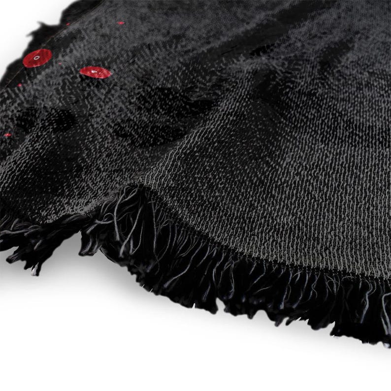 May include: A close-up of a black round beach towel with a fringed edge. The towel has a textured appearance and several red droplets are visible on the surface. The towel is made of a soft material.