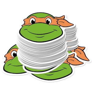 May include: A stack of stickers featuring a cartoon turtle head with an orange mask. The turtle has a green face, a smiling mouth, and white eyes. The stickers are white with a black outline and the Viacom logo.