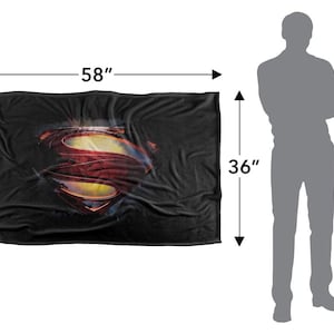Puede incluir: Una manta negra, de 147 cm de largo y 91 cm de ancho, con el logotipo de Superman en rojo, amarillo y azul. La manta es rectangular y parece suave, adecuada para usar como manta o cubierta.