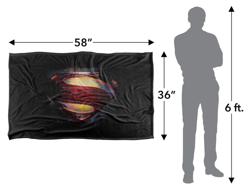Puede incluir: Una manta negra, de 147 cm de largo y 91 cm de ancho, con el logotipo de Superman en rojo, amarillo y azul. La manta es rectangular y parece suave, adecuada para usar como manta o cubierta.