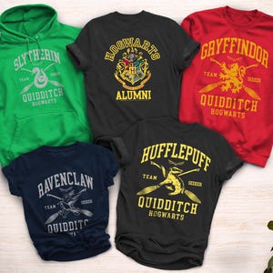 May include: A collection of apparel featuring designs inspired by the Hogwarts houses and Quidditch teams. Includes a green Slytherin hoodie, a black Hogwarts Alumni t-shirt, a red Gryffindor sweatshirt, a navy Ravenclaw t-shirt, and a black Hufflepuff t-shirt.