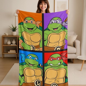 May include: A colorful blanket featuring the Teenage Mutant Ninja Turtles. The design is divided into four squares, each showcasing a turtle with a different colored mask: orange, purple, blue, and red. The turtles are green with tan shells.