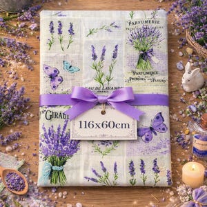 Peut inclure: Un tissu rectangulaire sur le thème de la lavande, 116cm x 60cm, avec des brins de lavande, des papillons et du texte. Un ruban violet avec un nœud entoure le tissu. Le tissu porte les inscriptions "Parfumerie" et "Sau de Lavande".