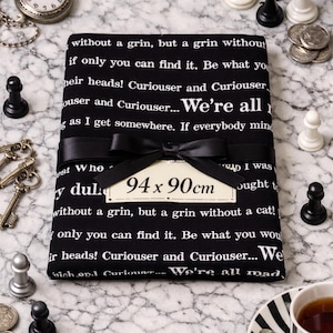 Peut inclure: Un tissu noir avec du texte blanc, noué avec un ruban noir et une étiquette indiquant "94 x 90cm". Des pièces d'échecs, des dés, une montre de poche, des clés, des pièces de monnaie et une tasse de thé sont disposés autour du tissu.