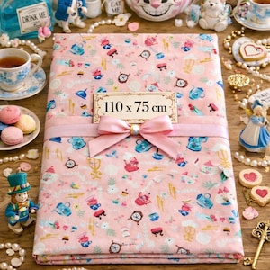 Peut inclure: Un tissu rose de 110 x 75 cm, sur le thème d'Alice au pays des merveilles, est présenté. Il est orné de tasses à thé, d'horloges et d'autres motifs fantaisistes. Un ruban et un nœud roses l'ornent. Divers objets décoratifs entourent le tissu.