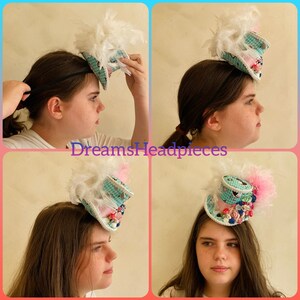 Puede incluir: Un peque&ntilde;o sombrero decorativo con un patr&oacute;n de cuadros turquesa y blanco, adornado con plumas blancas, detalles rosas y adornos florales. El sombrero se lleva en la cabeza. El texto "DreamsHeadpieces" es visible.