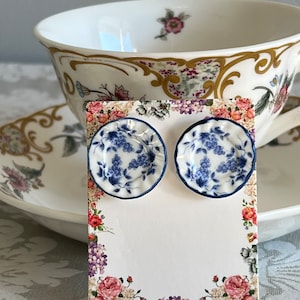 Peut inclure: Une paire de boucles d'oreilles en porcelaine bleu et blanc en forme de petites assiettes avec un motif floral. Les boucles d'oreilles sont présentées sur une carte avec une bordure florale.