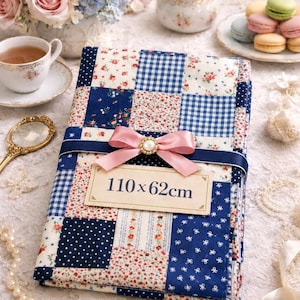 Peut inclure: Une courtepointe patchwork avec un motif floral et vichy bleu, blanc et rouge. La courtepointe mesure 110 x 62 cm et est attachée avec un ruban rose et une étiquette décorative qui indique "110 x 62cm".