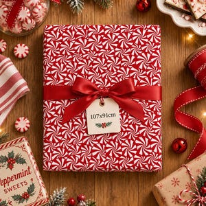 Peut inclure: Un cadeau rectangulaire emballé dans du papier à motif de tourbillons de menthe poivrée rouge et blanc, noué avec un ruban de satin rouge lisse et un nœud. Une étiquette crème attachée au ruban affiche le texte 107x91cm et un motif de houx.