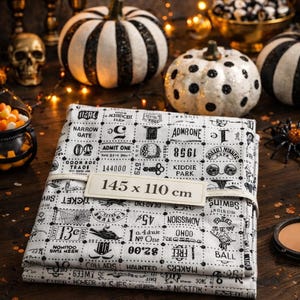 Peut inclure: Un tissu plié avec un motif de billets vintage, mesurant 145 x 110 cm, est au centre de l'image. Le tissu est blanc avec des textes et des illustrations noirs. Des citrouilles décoratives, des bougies et des objets sur le thème d'Halloween créent une ambiance festive.